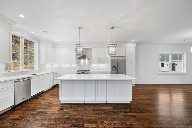 kitchen with sink, hanging light fixtures, wall chimney range hood, a kitchen island, and appliances with stainless steel finishes