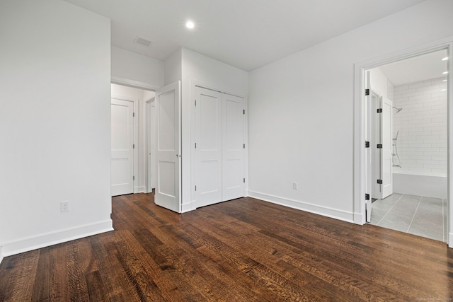 unfurnished bedroom featuring ensuite bathroom, a closet, and dark wood-type flooring