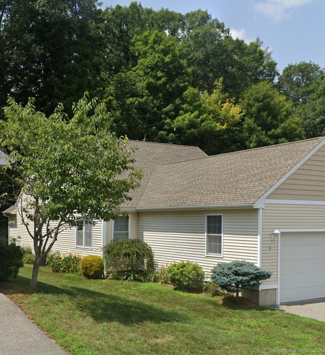 view of front of house with a shingled roof, an attached garage, driveway, and a front lawn