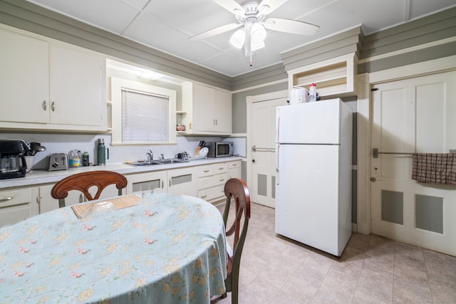 kitchen featuring a sink, white cabinetry, light countertops, freestanding refrigerator, and stainless steel microwave