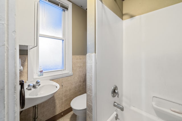 bathroom featuring shower / bath combination, tile walls, toilet, a wainscoted wall, and a sink