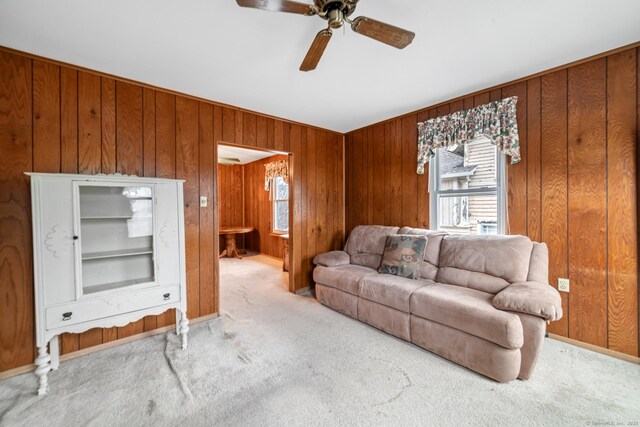 carpeted living room featuring ceiling fan and wooden walls