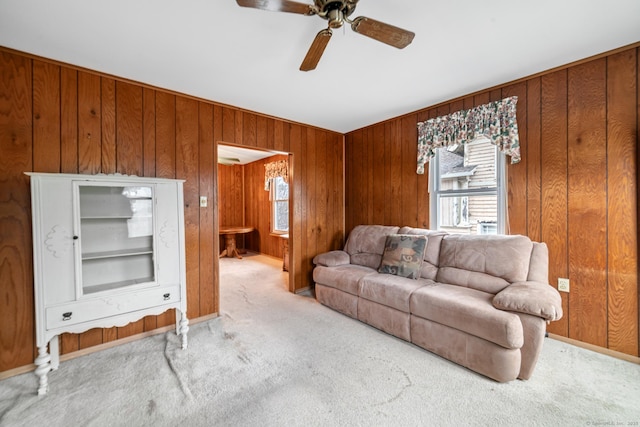 living room featuring a ceiling fan, light colored carpet, plenty of natural light, and wooden walls