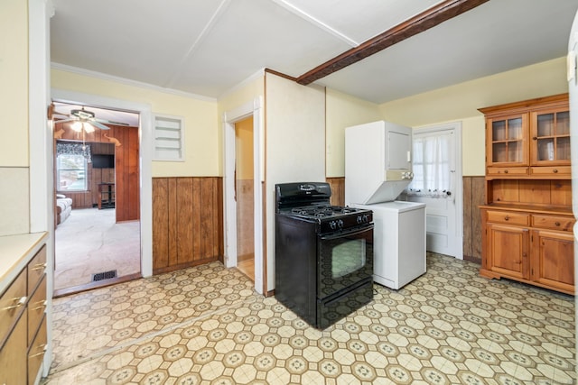 kitchen with wood walls, black range with gas stovetop, crown molding, ceiling fan, and stacked washer / drying machine