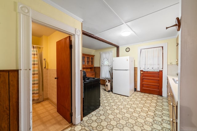 kitchen featuring black range oven, white refrigerator, and crown molding