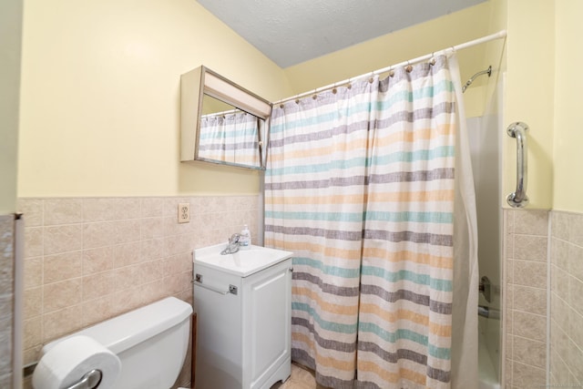 full bath featuring tile walls, a wainscoted wall, a textured ceiling, and vanity