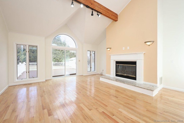 unfurnished living room with baseboards, high vaulted ceiling, a premium fireplace, beam ceiling, and light wood-style floors