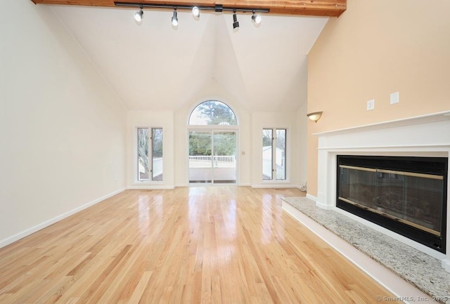 unfurnished living room featuring high vaulted ceiling, light hardwood / wood-style floors, rail lighting, and a high end fireplace