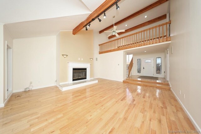 unfurnished living room with beamed ceiling, ceiling fan, and light hardwood / wood-style flooring