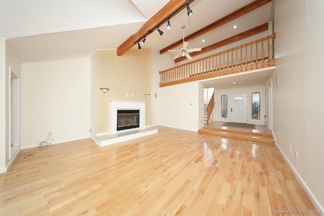 unfurnished living room with light wood-style flooring, ceiling fan, stairs, a glass covered fireplace, and beamed ceiling