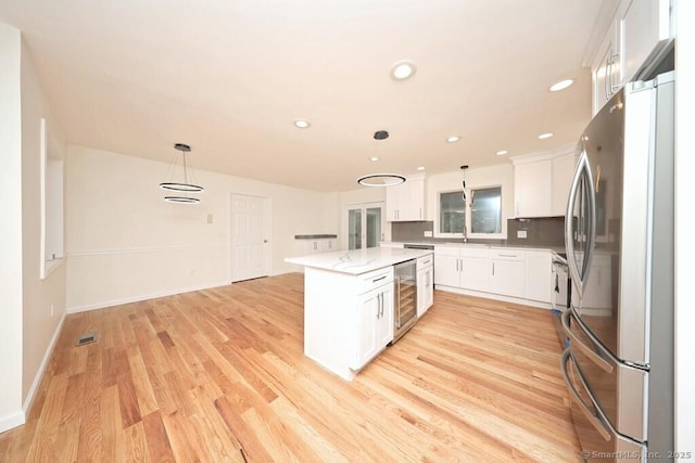 kitchen with beverage cooler, pendant lighting, freestanding refrigerator, light wood-style floors, and white cabinets