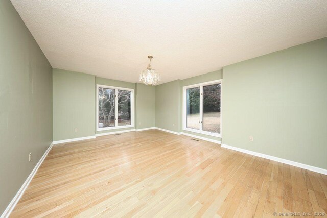 spare room featuring a chandelier, a textured ceiling, and light hardwood / wood-style floors