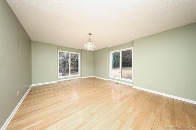 empty room featuring light wood-type flooring, baseboards, an inviting chandelier, and visible vents