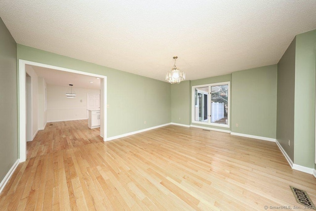 spare room with baseboards, visible vents, a textured ceiling, a notable chandelier, and light wood-type flooring