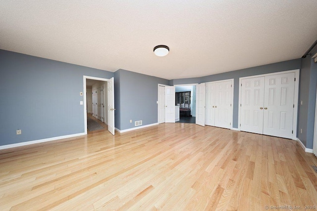 unfurnished bedroom featuring visible vents, light wood-style floors, baseboards, and two closets