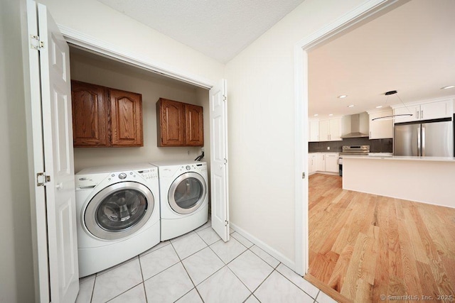 clothes washing area with washer and clothes dryer, light tile patterned floors, cabinet space, and baseboards