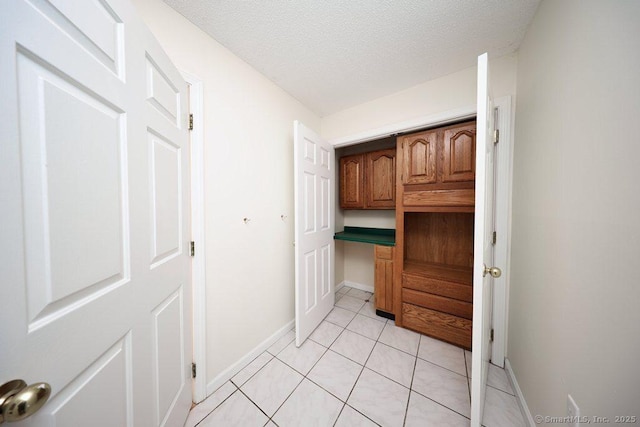 corridor with light tile patterned floors, baseboards, and a textured ceiling