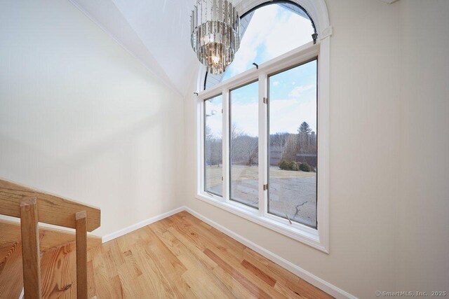 spare room featuring lofted ceiling, light wood-type flooring, and a chandelier