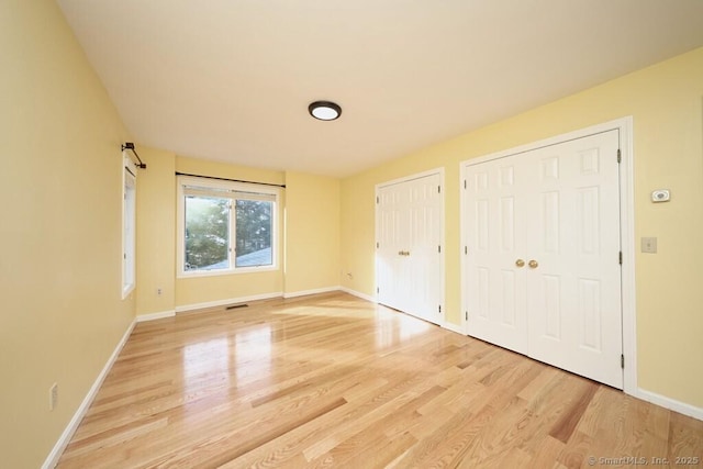 unfurnished bedroom featuring visible vents, light wood-style flooring, two closets, and baseboards