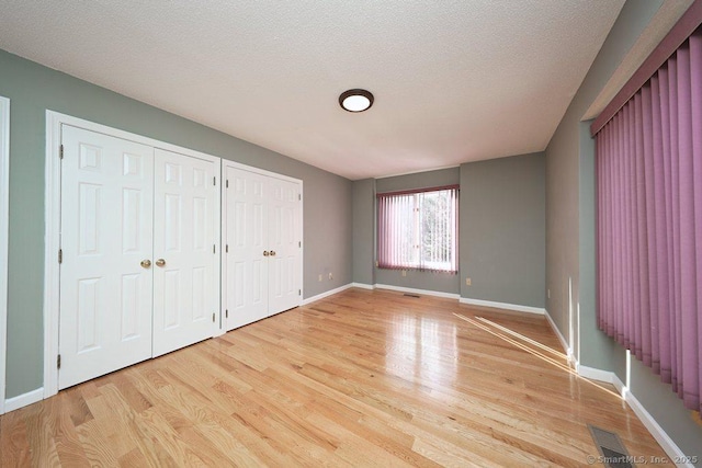 unfurnished bedroom with visible vents, two closets, baseboards, light wood-style flooring, and a textured ceiling