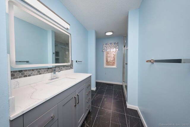 bathroom with a textured ceiling, vanity, a shower with shower door, and backsplash