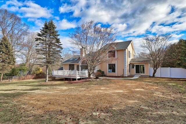 rear view of property featuring a deck, a yard, fence, and a chimney