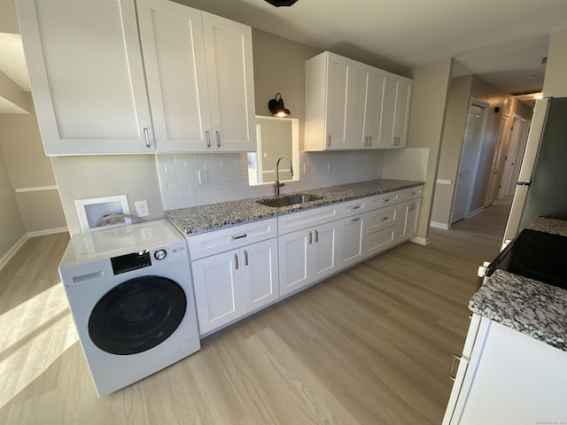 laundry room featuring washer / clothes dryer, sink, cabinets, and light hardwood / wood-style flooring