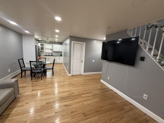 living room featuring baseboard heating, ceiling fan, sink, and light hardwood / wood-style floors