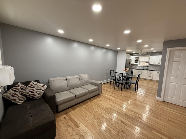 living room featuring baseboard heating, ceiling fan, and light hardwood / wood-style flooring