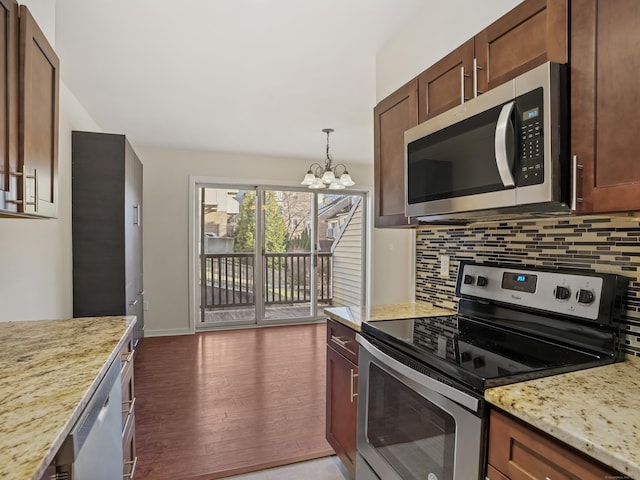 kitchen with stainless steel appliances, light stone counters, a notable chandelier, pendant lighting, and decorative backsplash