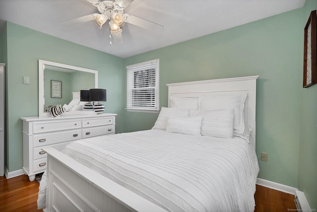 bedroom with dark wood-type flooring, ceiling fan, and a baseboard heating unit