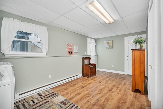 interior space with light wood-type flooring, a drop ceiling, washer and clothes dryer, a baseboard heating unit, and plenty of natural light