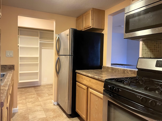 kitchen featuring light brown cabinetry, stainless steel appliances, and a textured ceiling