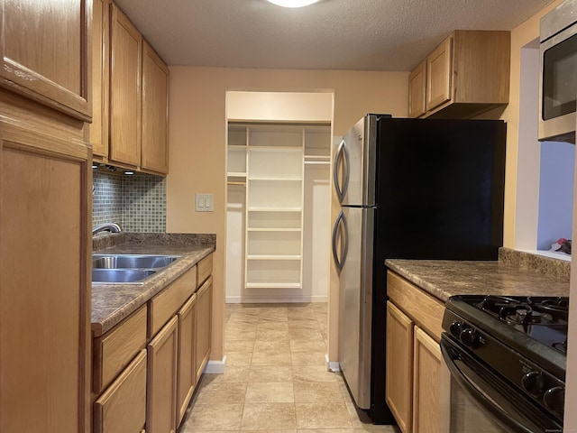 kitchen with sink, light tile patterned floors, a textured ceiling, appliances with stainless steel finishes, and tasteful backsplash