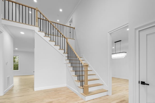 stairway with a chandelier, wood-type flooring, and ornamental molding