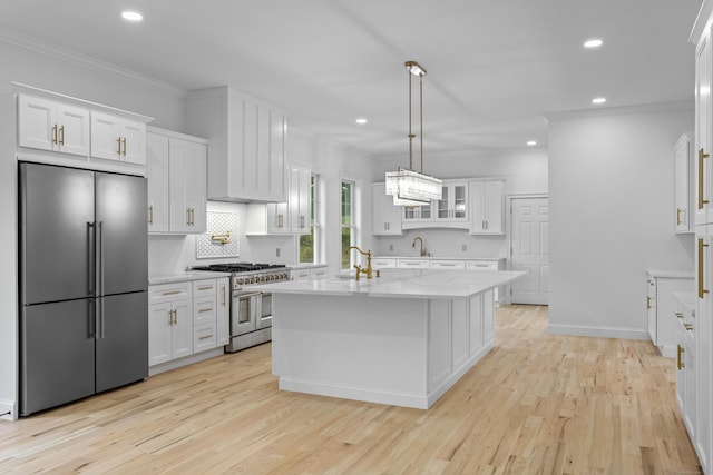 kitchen featuring appliances with stainless steel finishes, light wood-type flooring, a center island with sink, decorative light fixtures, and white cabinets