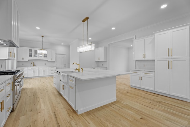 kitchen featuring white cabinetry, sink, hanging light fixtures, a kitchen island with sink, and stainless steel stove