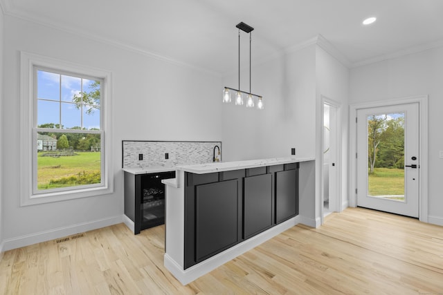 kitchen with kitchen peninsula, decorative light fixtures, crown molding, and a healthy amount of sunlight