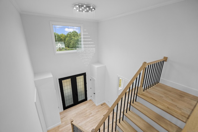 entrance foyer with crown molding, french doors, light hardwood / wood-style floors, and an inviting chandelier