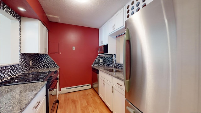 kitchen with white cabinets, light wood-type flooring, baseboard heating, appliances with stainless steel finishes, and light stone counters