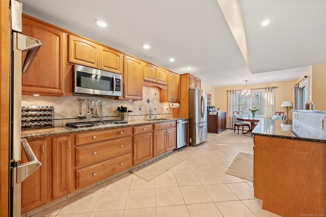 kitchen with a notable chandelier, dark stone counters, decorative backsplash, light tile patterned flooring, and appliances with stainless steel finishes