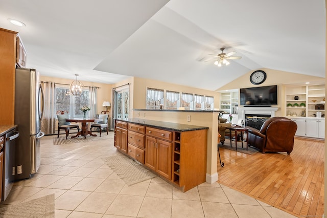 kitchen with hanging light fixtures, dark stone counters, light tile patterned floors, ceiling fan with notable chandelier, and appliances with stainless steel finishes