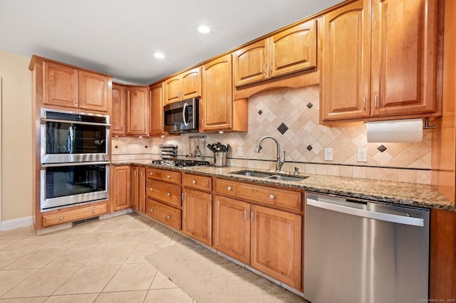 kitchen with light stone countertops, sink, decorative backsplash, light tile patterned floors, and appliances with stainless steel finishes