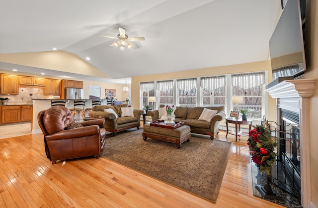 living room featuring ceiling fan with notable chandelier, lofted ceiling, sink, and light hardwood / wood-style flooring