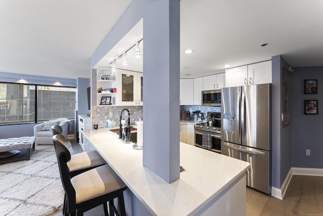 kitchen with decorative backsplash, appliances with stainless steel finishes, white cabinetry, kitchen peninsula, and a breakfast bar area