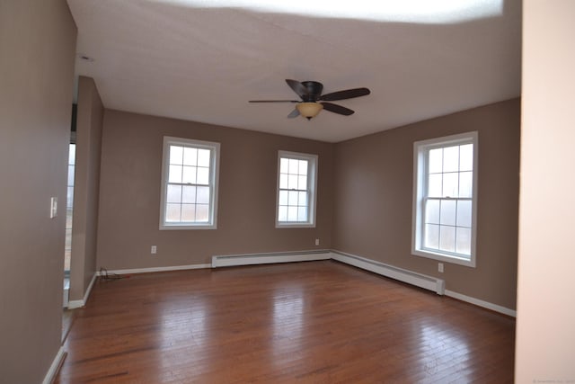 empty room featuring wood-type flooring, a wealth of natural light, ceiling fan, and a baseboard heating unit