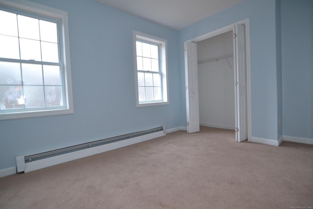 unfurnished bedroom with light carpet, a closet, and a baseboard heating unit