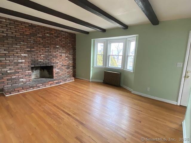 unfurnished living room with beam ceiling, radiator, light hardwood / wood-style flooring, and a brick fireplace