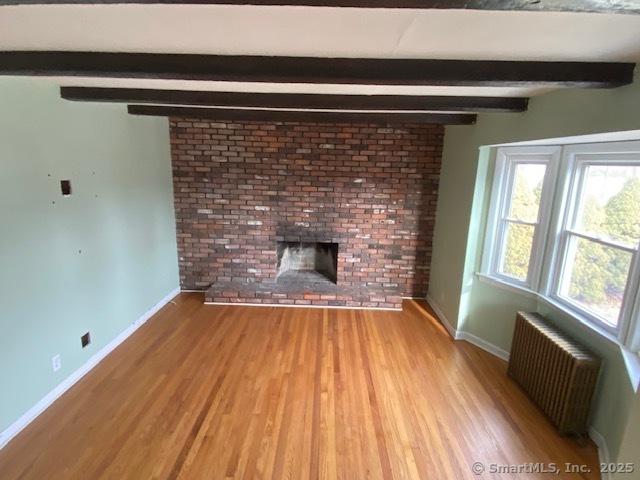 unfurnished living room with a fireplace, radiator heating unit, beamed ceiling, and light hardwood / wood-style flooring