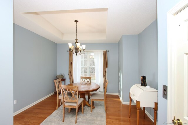 dining area featuring a tray ceiling, wood-type flooring, and a notable chandelier